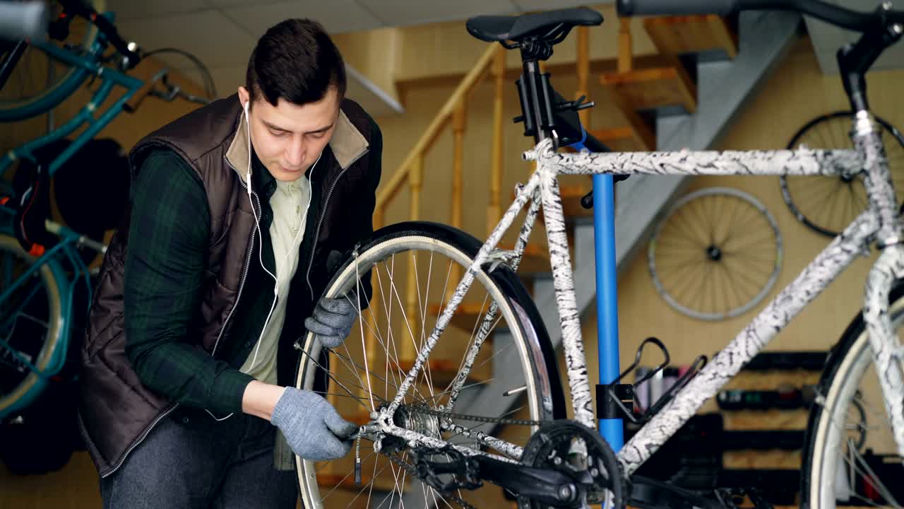 mecánico experimentado está montando bicicleta ajustando la rueda trasera durante el mantenimiento del vehículo en el lugar de trabajo. instrumentos profesionales, piezas de repuesto y equipos son visibles.