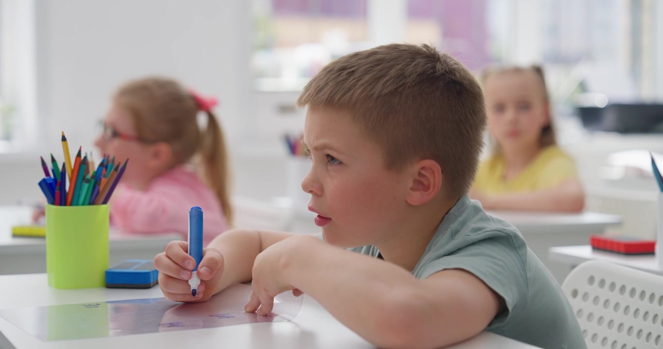 Niño concentrado escribiendo con rotulador en el pupitre escolar