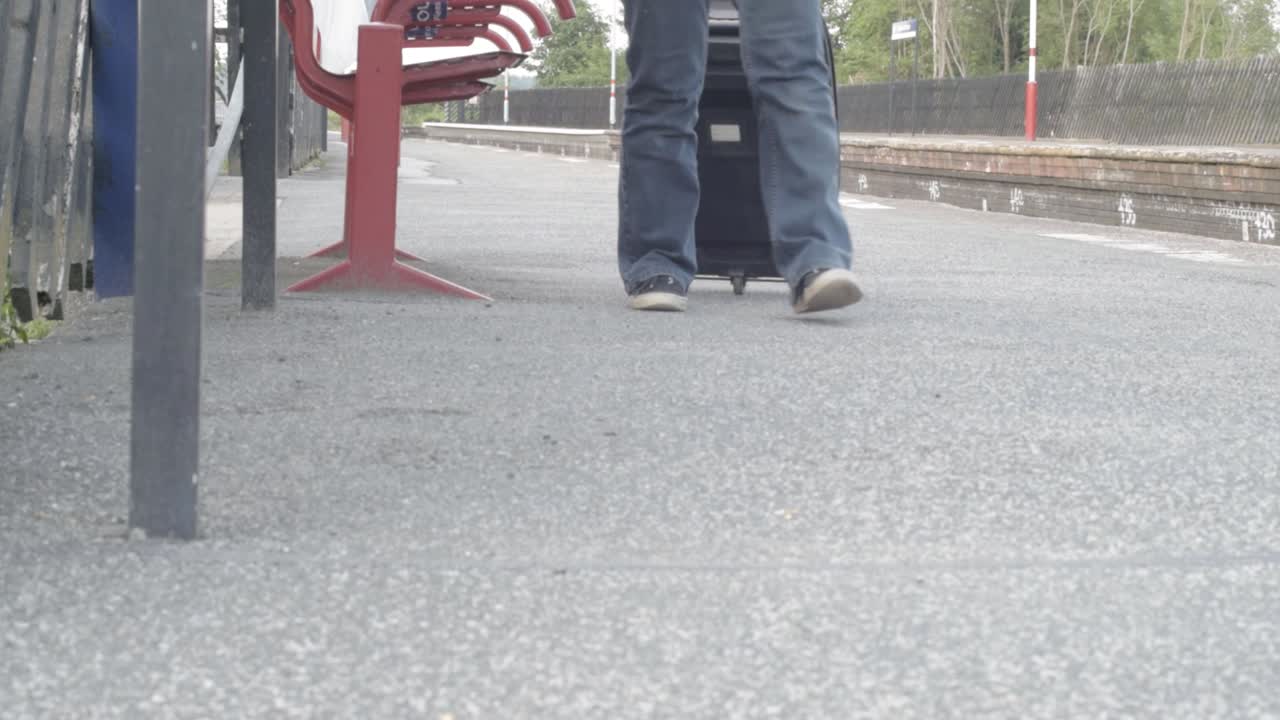 Wheeling suitcase towards camera on train platform wide shot