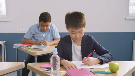 male student sitting at desk in english classroom writting in her notebook