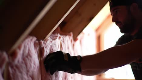 a skilled worker carefully installs insulation material in a residential attic. natural light filters through, illuminating the careful craftsmanship required for efficient energy use in homes.