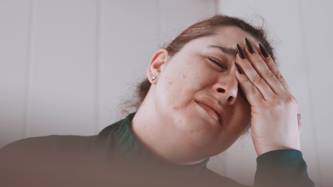 Donna tranquilla e stanca. Una donna a riposo mostra stanchezza e concentrazione. Una donna con un maglione verde appare esausta e attenta. Una donna serena seduta in una stanza tranquilla mostra fatica e concentrazione.