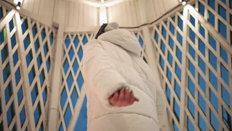 young girl dancing passionately with eyes closed inside illuminated lattice gazebo at dusk wearing white puffer coat beanie and headphones snow visible beyond pavilion conveying emotional rhythm