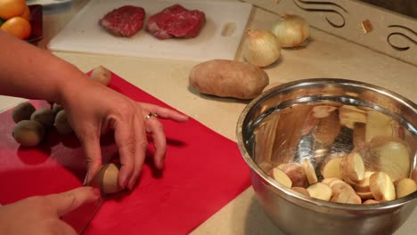 mujer cortando papas para bebés con cuchillo de chef y tabla de cortar roja
