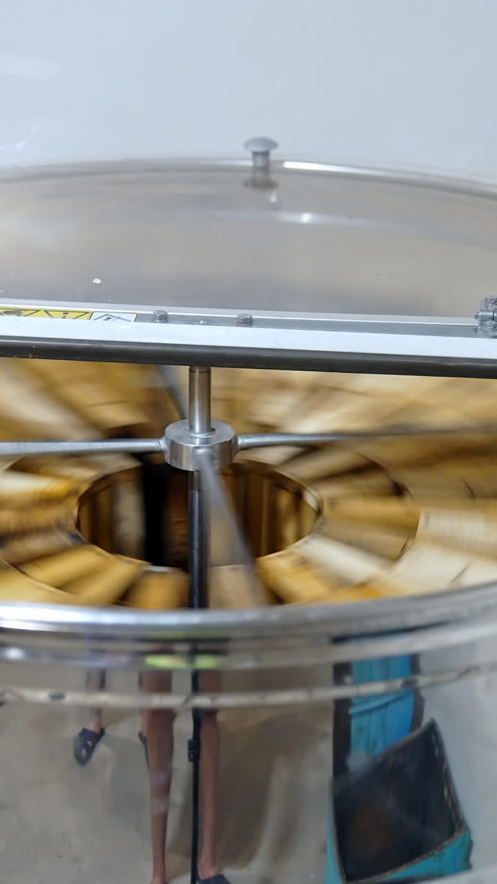Metal centrifugal machine pumping organic honey. Honey extractor is spinning with frames to press out honey from honeycombs. Vertical video