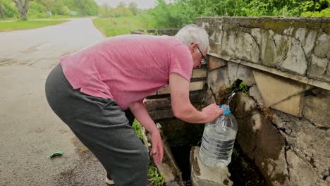 man fills bottle with free natural mineral water from village spring well supply