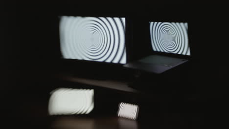 Angled-shot-of-a-hypnotic-spiral-pattern-displayed-on-four-device-screens-in-a-dark-room-with-selective-focus-and-a-choppy-shutter-speed-effect