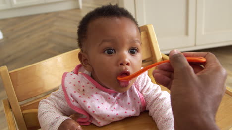 father feeds baby daughter in high chair shot in slow motion