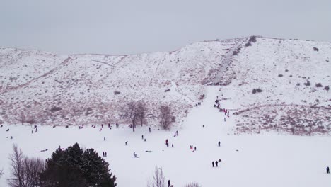 Toma-De-Drones-De-Personas-Jugando-En-Una-Colina-Cubierta-De-Nieve-Durante-El-Invierno