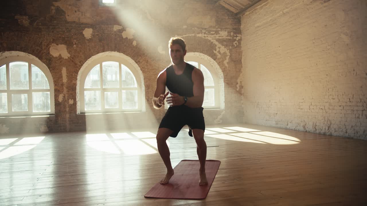 A man does exercises and squats in a sunny gym on a special carpet for sports. Doing sports in the sunny gym workout in the morning