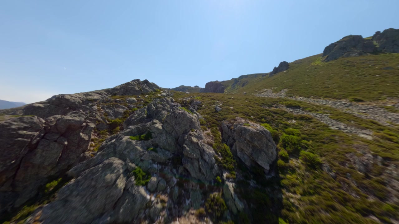 Ripresa dinamica con drone FPV che si libra rapidamente sopra cime rocciose illuminate dal sole e pendii scoscesi a Puerto San Isidro, Asturie, Spagna. Luce diurna nitida, ampia vista paesaggistica, senza persone, dettagli naturali vibranti