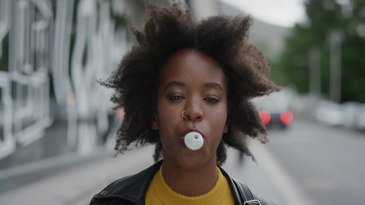 retrato de una joven afroamericana soplando chicle dulce disfrutando de diversión juguetona estudiante negra afro funky en la calle de la ciudad urbana