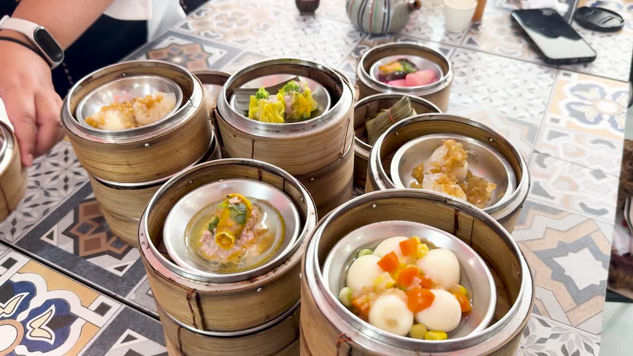 Tangan menata keranjang dim sum bambu di atas meja berpola, pencahayaan alami, sudut kamera dari atas