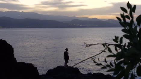 Joven-Viendo-La-Puesta-De-Sol-En-El-Mar-En-Un-Día-Nublado-Y-Mirando-A-Lo-Lejos-Mientras-Se-Siente-Inspirado