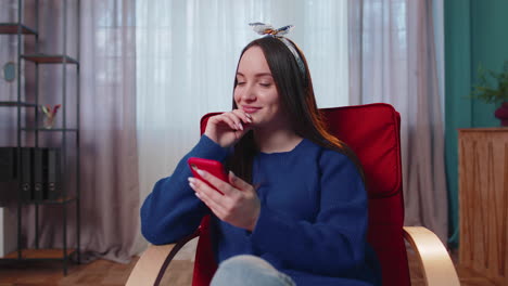 Cheerful-young-woman-sitting-on-chair,-using-mobile-phone-share-messages-on-social-media-application