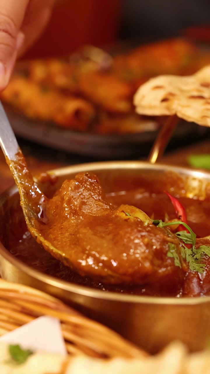 Primo piano di una mano che raccoglie denso curry di carne da una ciotola di ottone in un ristorante di Bangkok