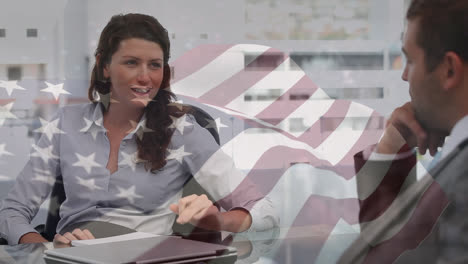 Waving-american-flag-against-diverse-businessman-and-businesswoman-discussing-at-office