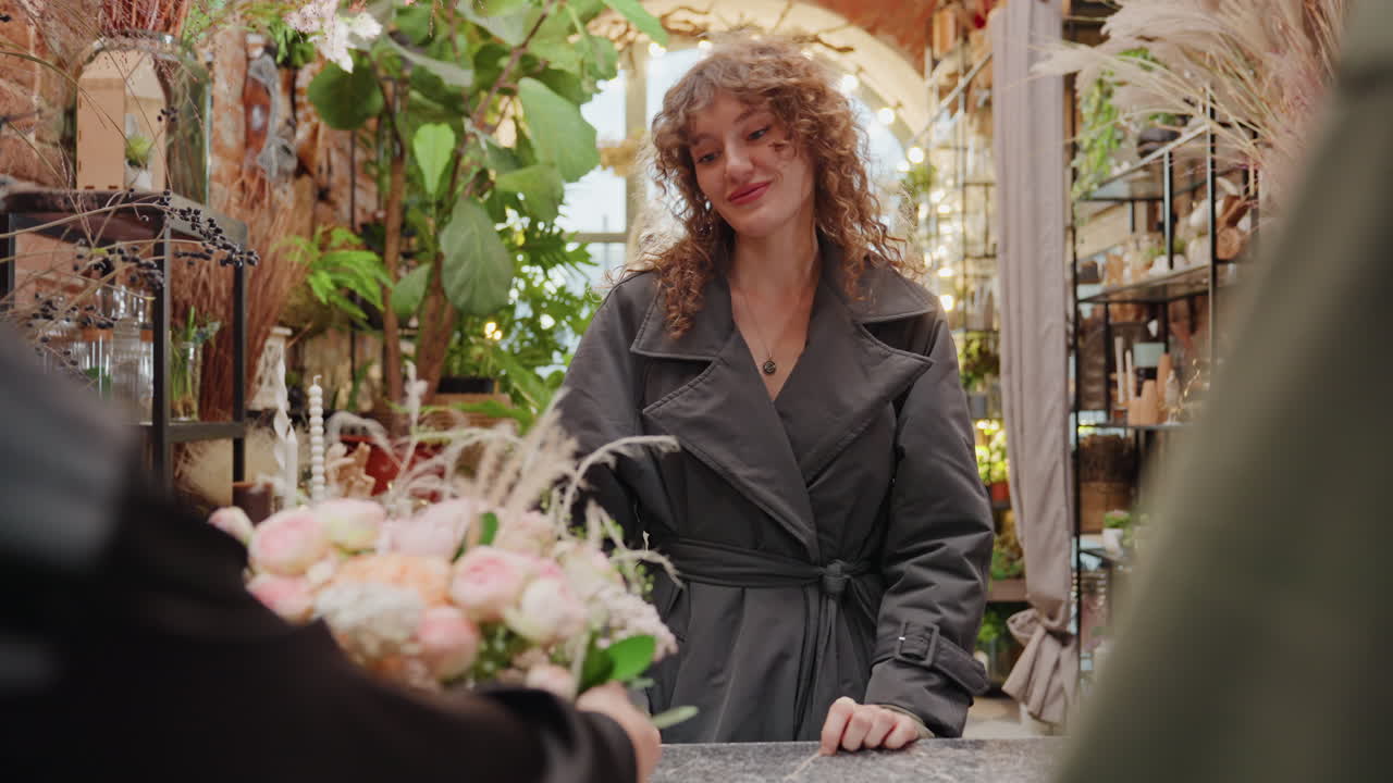 Fleuriste présentant un délicat bouquet de mariage, remise souriante à une cliente satisfaite au comptoir de la boutique. Vases et bougies allumées en arrière-plan, douces touches finales et ambiance de célébration avec des fleurs fraîches.