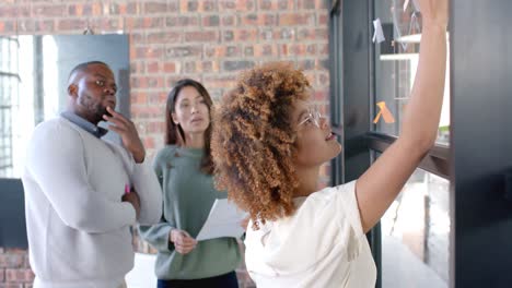 diverse male and female colleagues in discussion, brainstorming at glass wall in office, slow motion