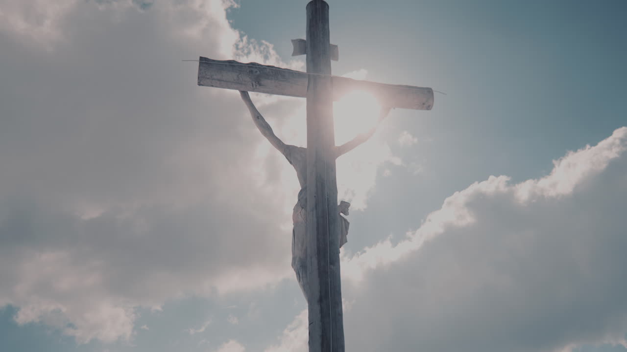 Heligt träkors belyst av solen mot himmelsbakgrund, den korsfäste Jesus Kristus.