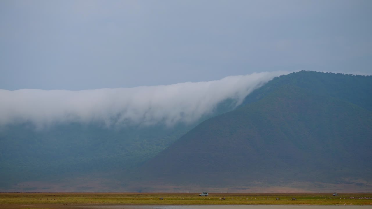 Safari vehicle driving through the heart of the Ngorongoro Crater early in the morning, with clouds drifting over the crater rim