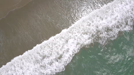 cenital drone shot flying straight up over the splashing waves at the beach in playas general villamil, ecuador