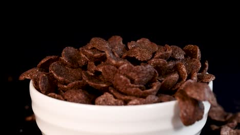 chocolate cereal flakes cascade into a white bowl against a black backdrop, creating a dynamic and appetizing visual