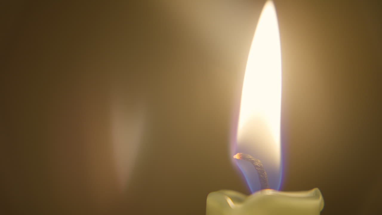 Una singola fiamma di candela che arde luminosamente, con uno stoppino incandescente a fuoco e uno sfondo sfumato caldo.