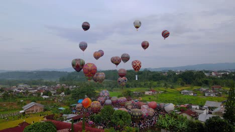 Aerial-view-of-colorful-air-balloon-are-floating-in-the-air-over-a-field-with-full-of-spectators