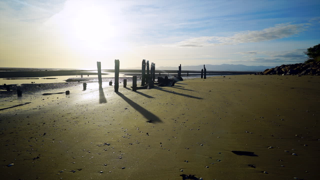 lapso de tiempo de largas sombras de postes de madera moviéndose sobre la playa durante la puesta de sol