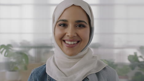 close up portrait of young muslim business woman looking at camera smiling confident wearing traditional hajib headscarf in office workspace background