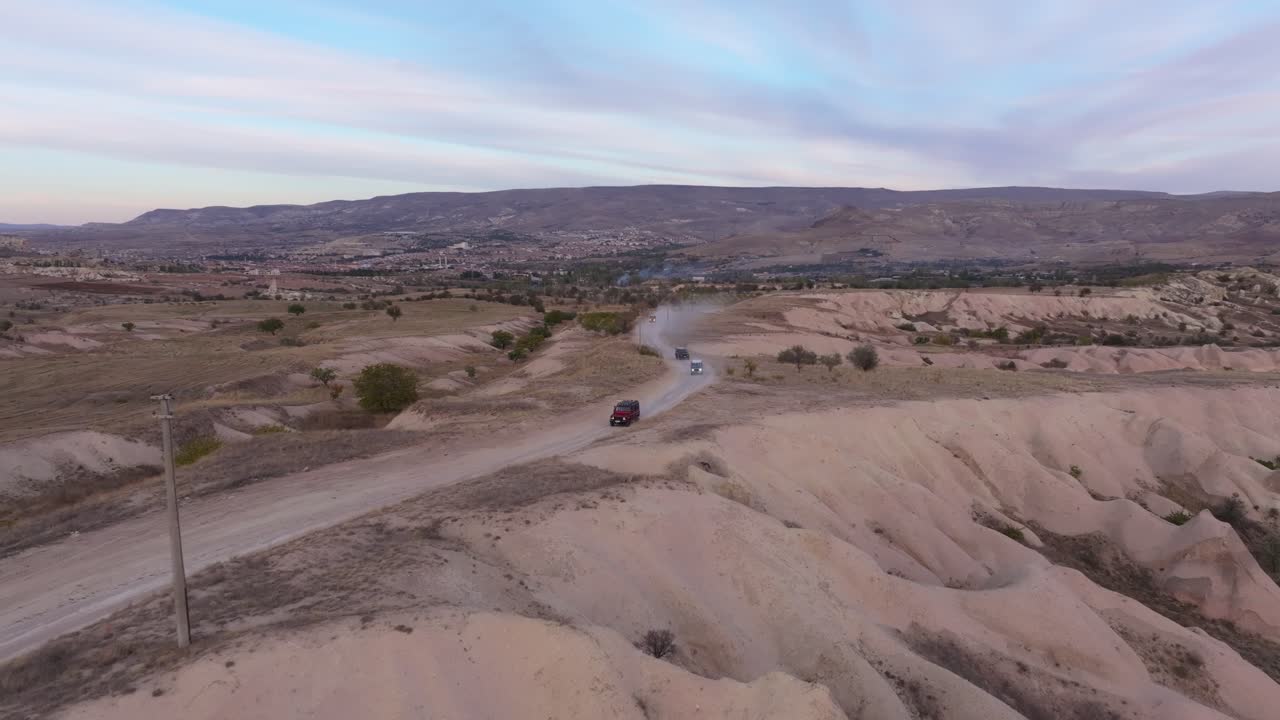 Veicoli fuoristrada che attraversano una valle con formazioni rocciose al tramonto, Turchia