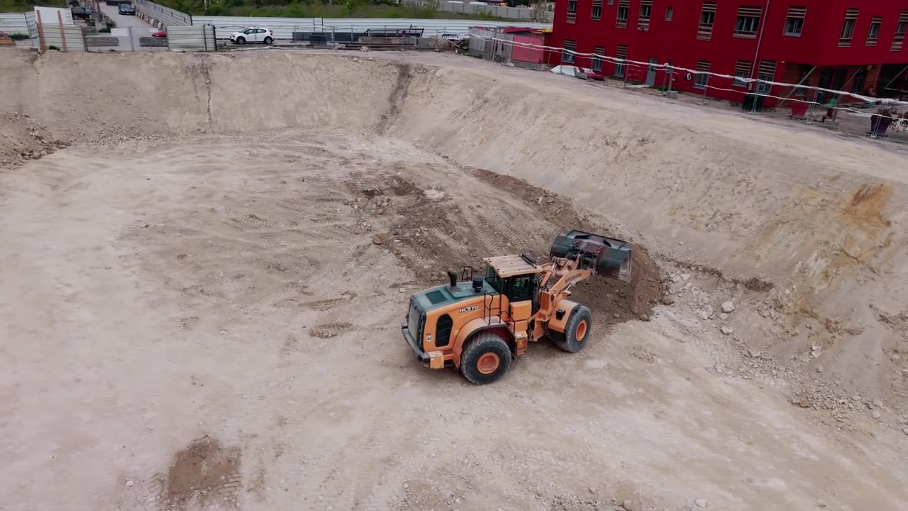 Pala gommata che sposta terra e terreno in una grande fossa in cantiere. Ripresa con drone.