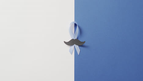 Video-of-paper-moustache-and-pale-blue-prostate-cancer-ribbon-on-white-and-blue-background