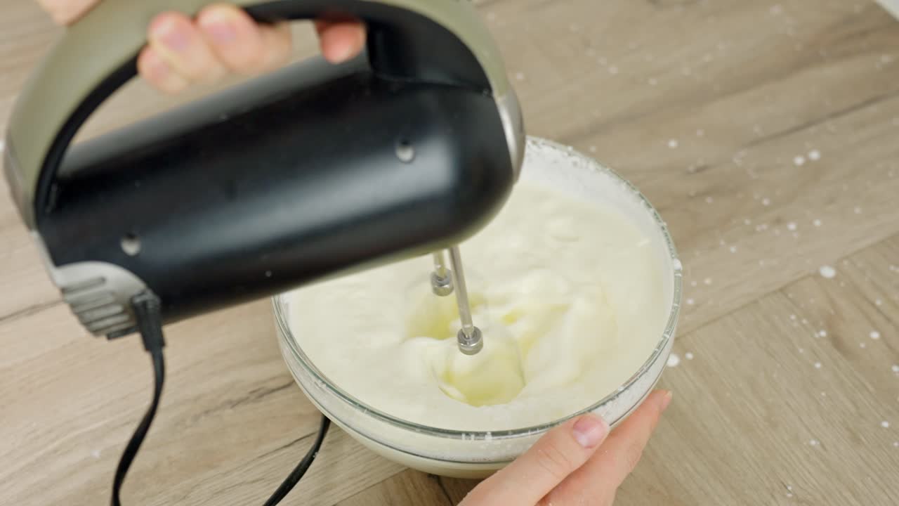 Blending thick cream mixture in bowl using electric hand mixer for dessert, splatter onto table
