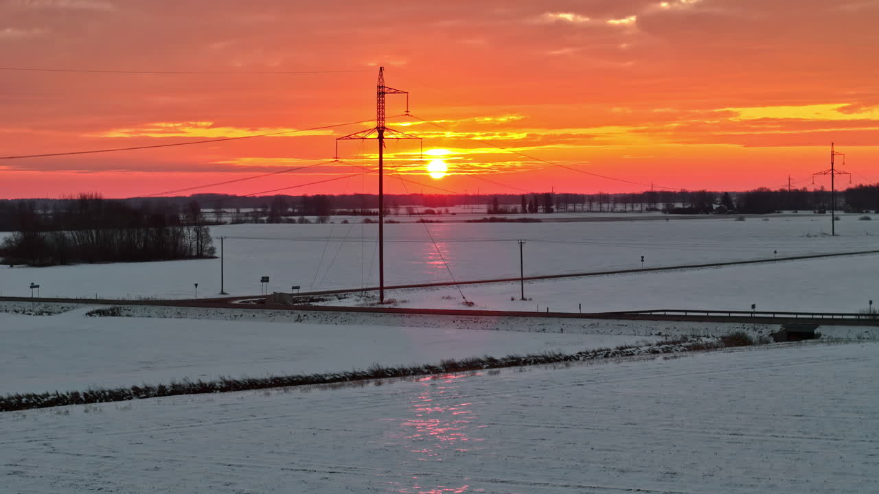 Luftfoto av et snødekt vinterlandskap under en oransje soloppgang