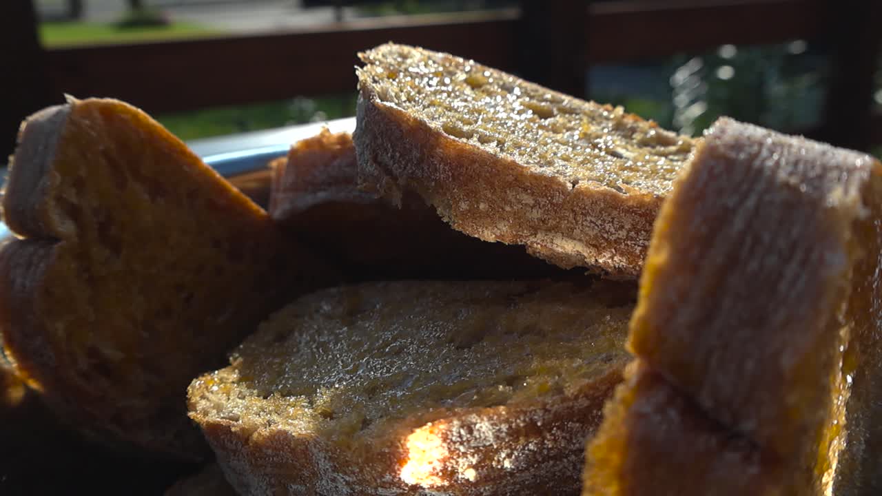 Gorgeous close up or closeup footage of hand adding oiled and golden ciabatta bread slices into a metal shiny bowl during a sunny summer day, preparing the bread for grilling or cooking, delicious