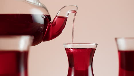 red liquid being poured from a glass teapot into a cup