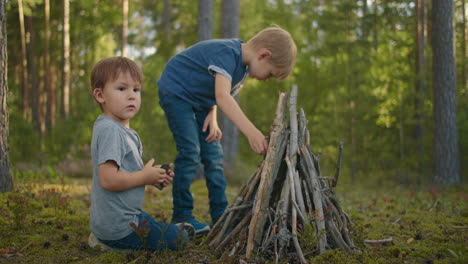 two boys put sticks in a fire in the woods during a hike. boys in the woods prepare to light a fire and put sticks together