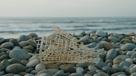 discarded fish trap on pebble beach, trash on the beach