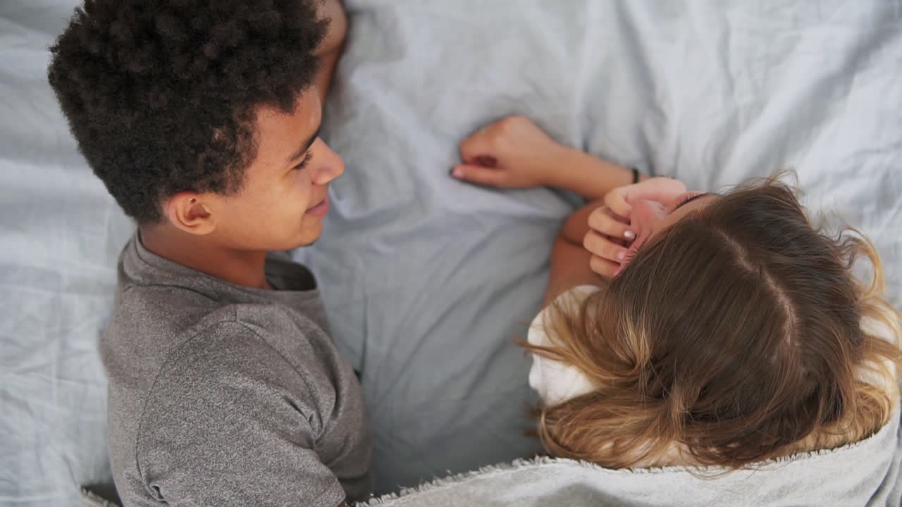 Top view of happy multiracial couple lying in bed and talking. Attractive young man and woman in love. Romantic concept