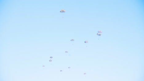 group of parachutists in mid-descent form a coordinated pattern against a bright blue sky during a military skydiving exercise