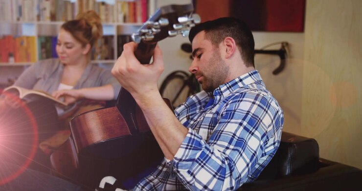 Un chitarrista preme i tasti e strimpella accordi in una stanza per un tutorial di musica mentre il partner legge.