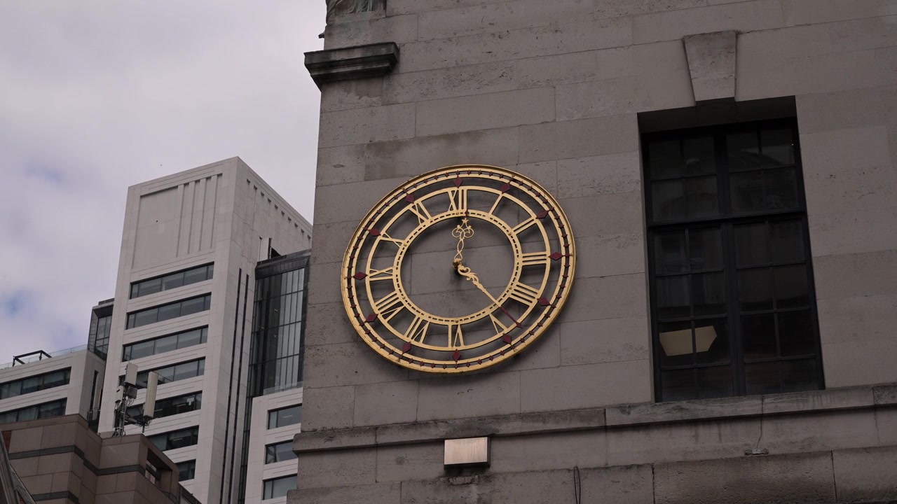 Gold Roman numeral clock on the NatWest Bank Moorgate facade with modern office buildings in the background under cloudy daylight.