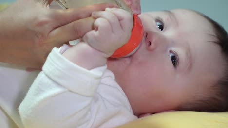 hungry baby lying on back feeding milk on bottle hold by her mother