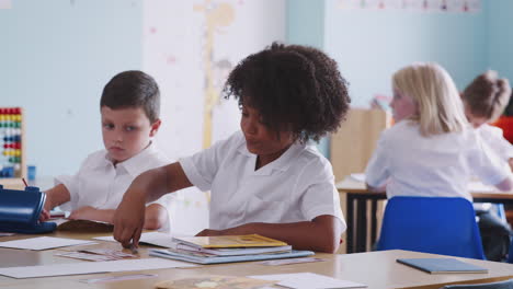 Grupo-De-Alumnos-De-Primaria-Vestidos-De-Uniforme-Trabajando-Juntos-En-Escritorios