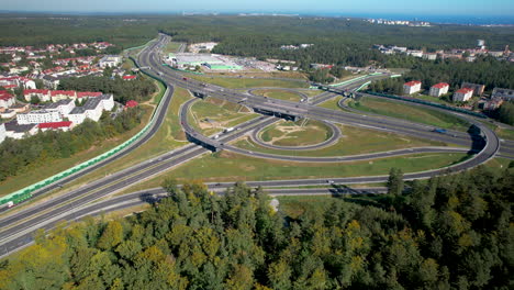 An-aerial-view-of-a-busy-intersection-near-Wielki-Kack,-Gdynia,-surrounded-by-residential-areas-and-woods-on-a-clear-day