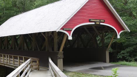 a red covered bridge sits on a road beside a wooden walkway in front of a forest