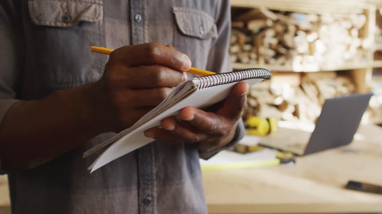 Mid section of african american male carpenter taking notes in a carpentry shop