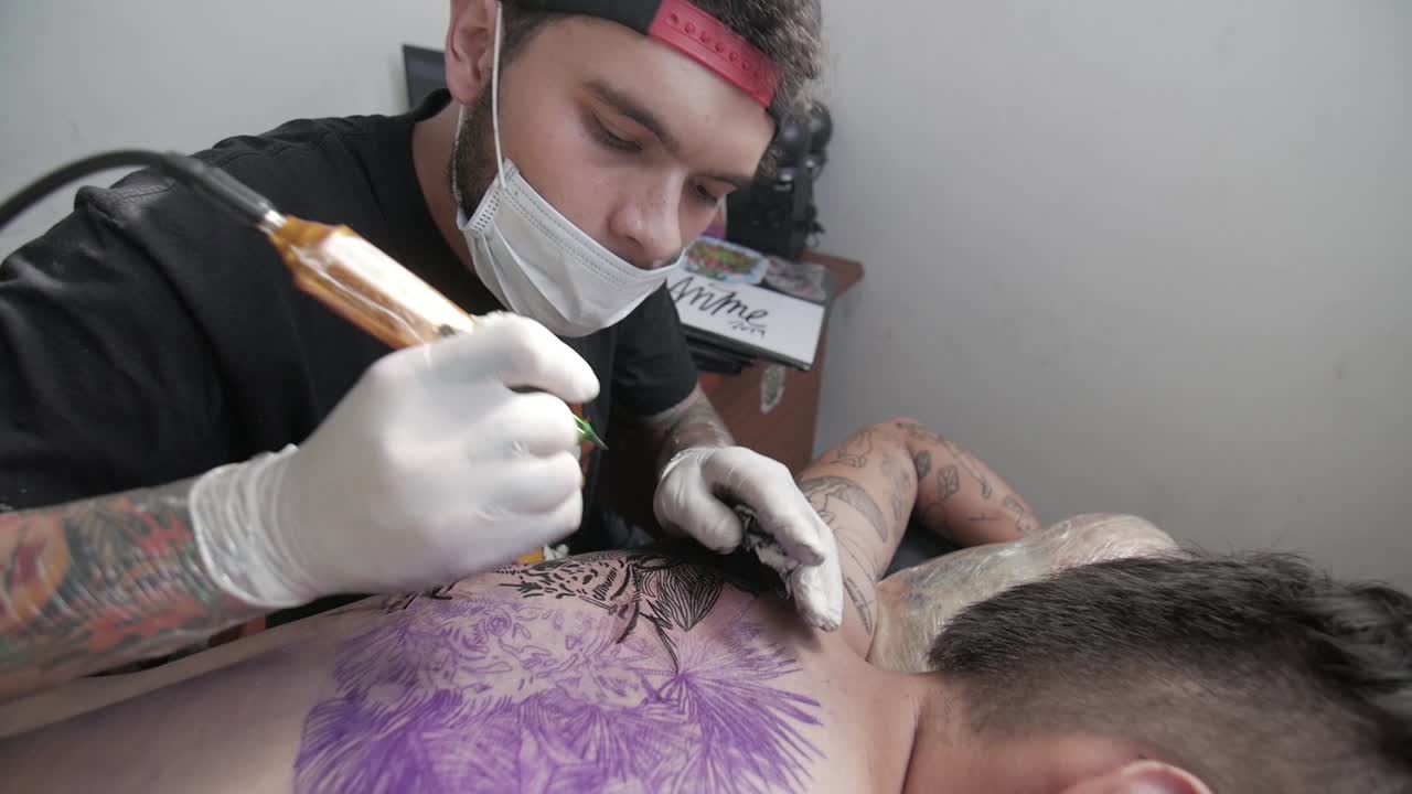 татуировщик чистит и проверяет ход татуировки